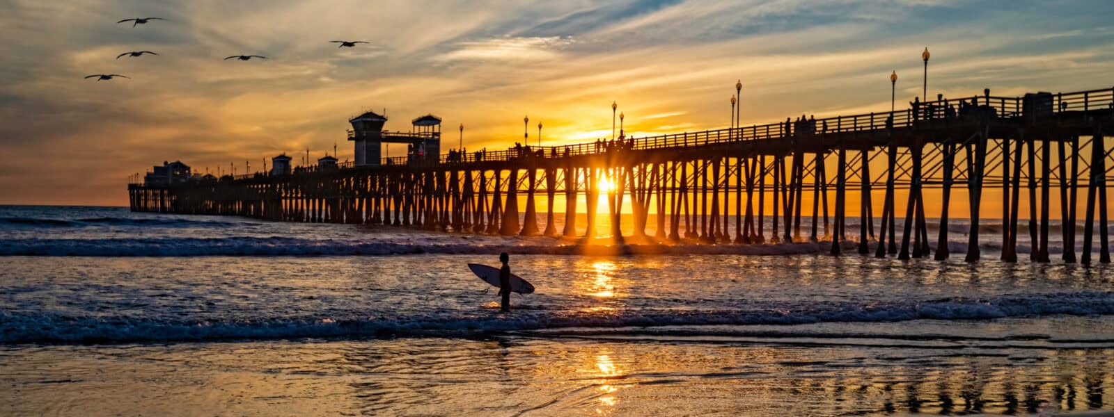 Surfer At Oceanside Pier A Colorful Sunset Image With Reflections And Pelicans Passing