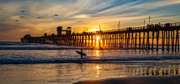 Surfer At Oceanside Pier A Colorful Sunset Image With Reflections And Pelicans Passing